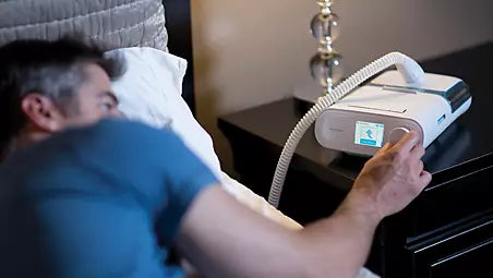 Patient using on-board performance check feature of Philips Respironics DreamStation Auto CPAP by the bedside.